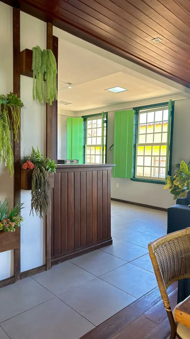 Zona común con mostrador de madera, plantas y ventanas con persianas verdes
