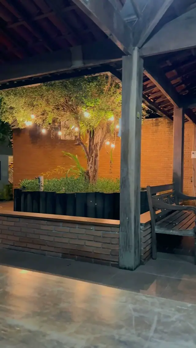 Patio con árbol, ladrillos, bancos y luces encendidas por la noche